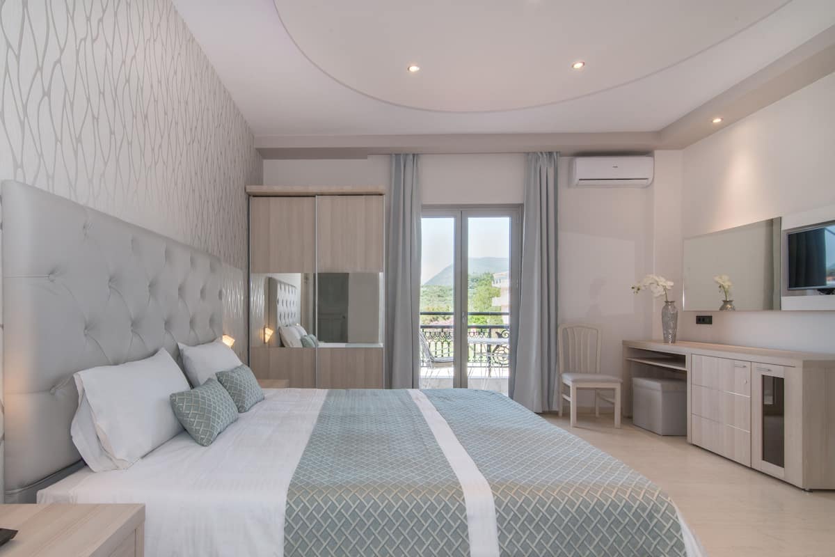 A modern hotel room with a large bed, a desk, a TV, and a balcony with a view.