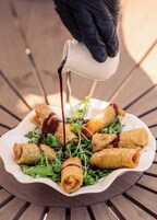 A plate of spring rolls with a sauce being poured over them.