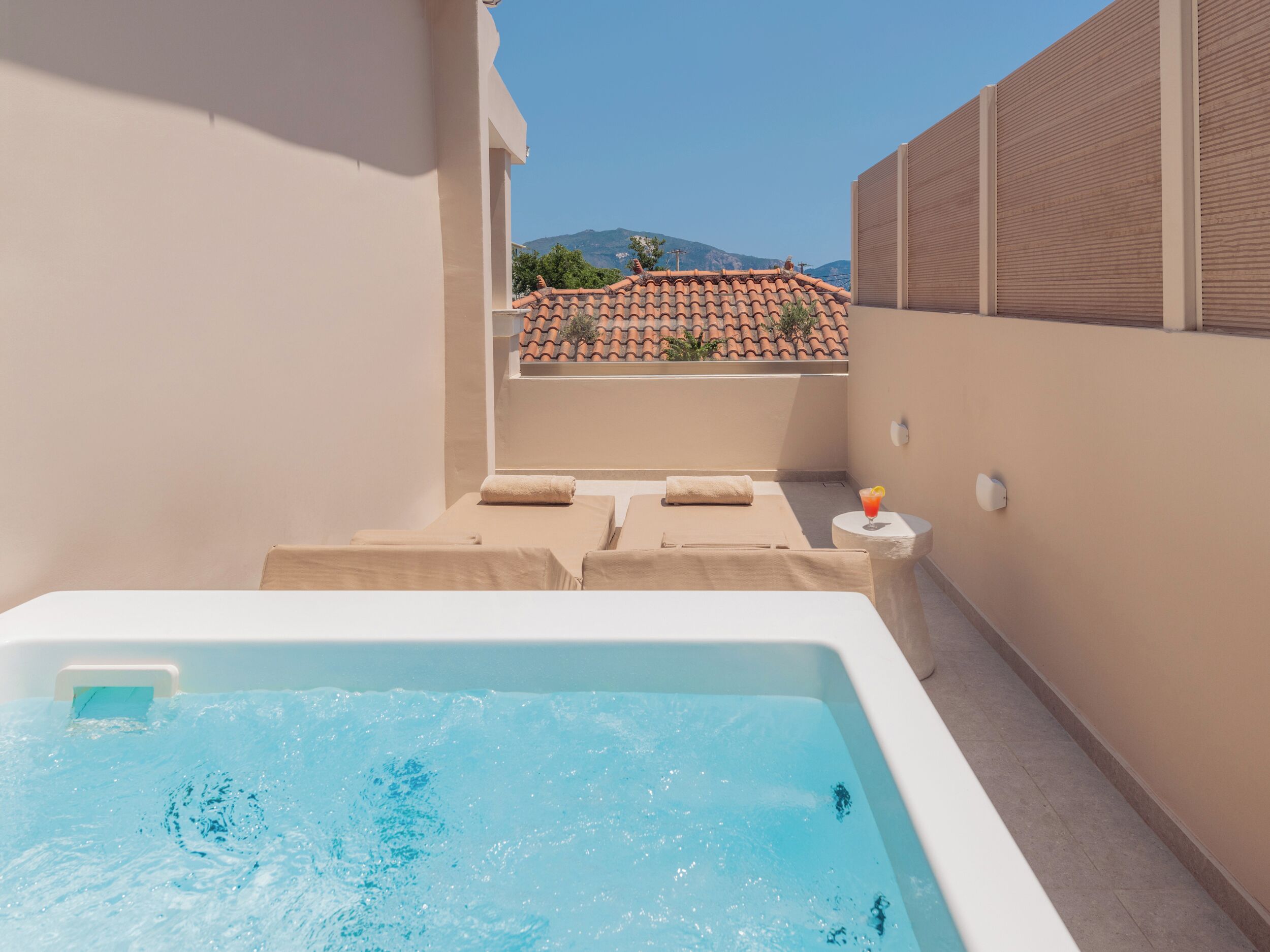 A spa area with a hot tub, lounge chairs, and a view of a tiled roof and mountains in the background.