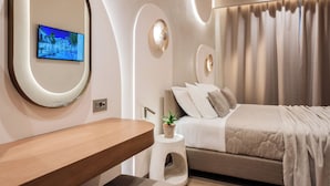 Een moderne slaapkamer met een bed, een nachtkastje, een spiegel en een aan de muur bevestigde televisie.