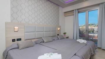 Een moderne hotelkamer met een groot bed, een hoofdeinde met ingebouwde verlichting, uitzicht op de stad en een balkon met tuinmeubilair.