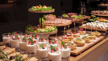 Un buffet con diverse pietanze, tra cui dolci, panini e un'elegante presentazione a tre piani di insalate.