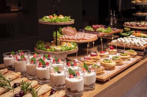 Un buffet con diverse pietanze, tra cui dolci, panini e un'elegante presentazione a tre piani di insalate.