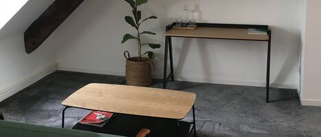 Een gezellig zolderkamertje met een schuine kap, een flatscreen televisie aan de muur, een klein houten tafeltje, een groene bank en een plant in pot.