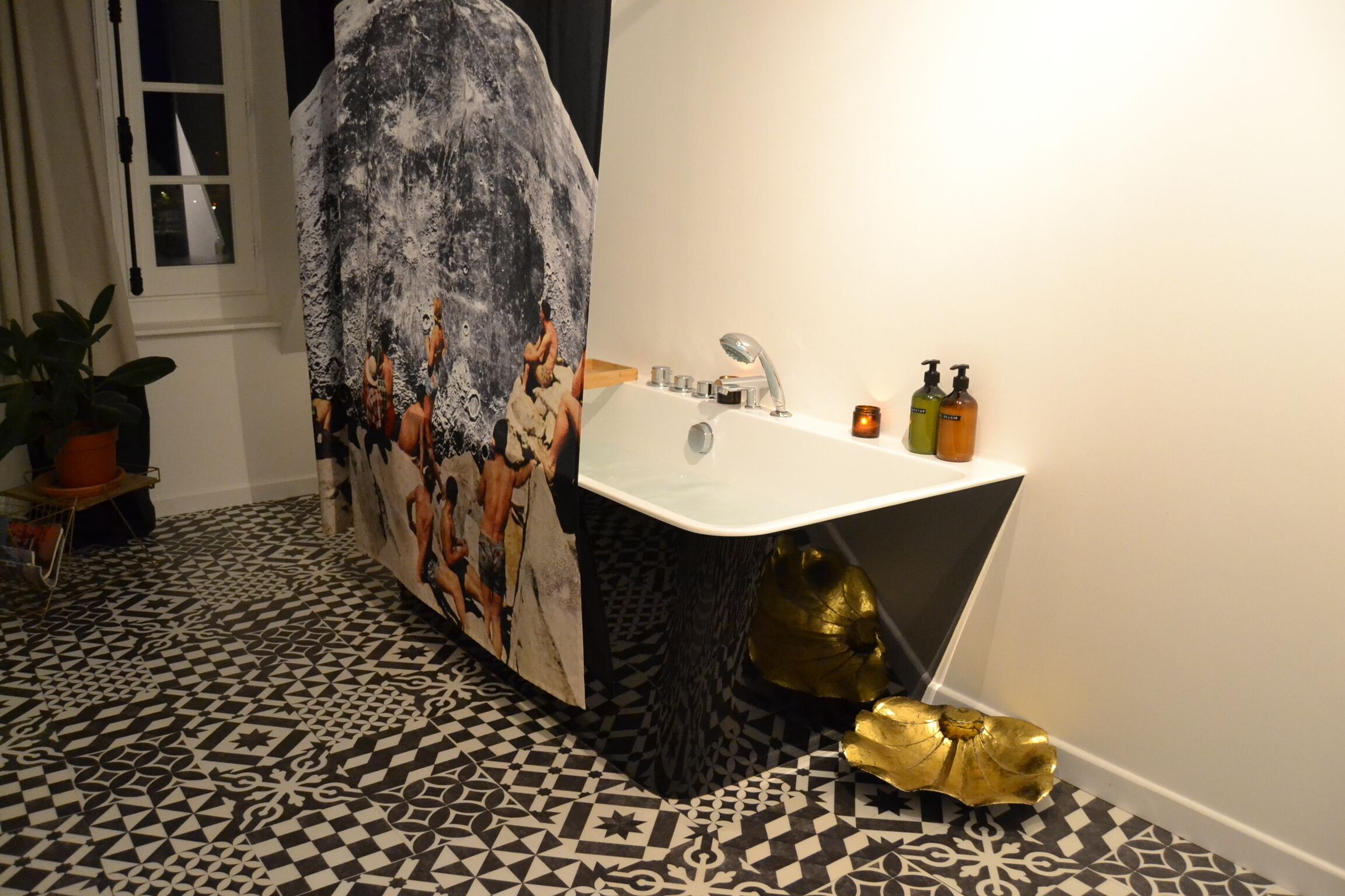 A bathroom with a black and white patterned floor, a white sink with a modern faucet, and a decorative gold object on the floor.