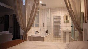 A hotel room with a large bed, a bathroom with a bathtub, a sink, and a mirror. - Artefact (Lamballe-Armor)