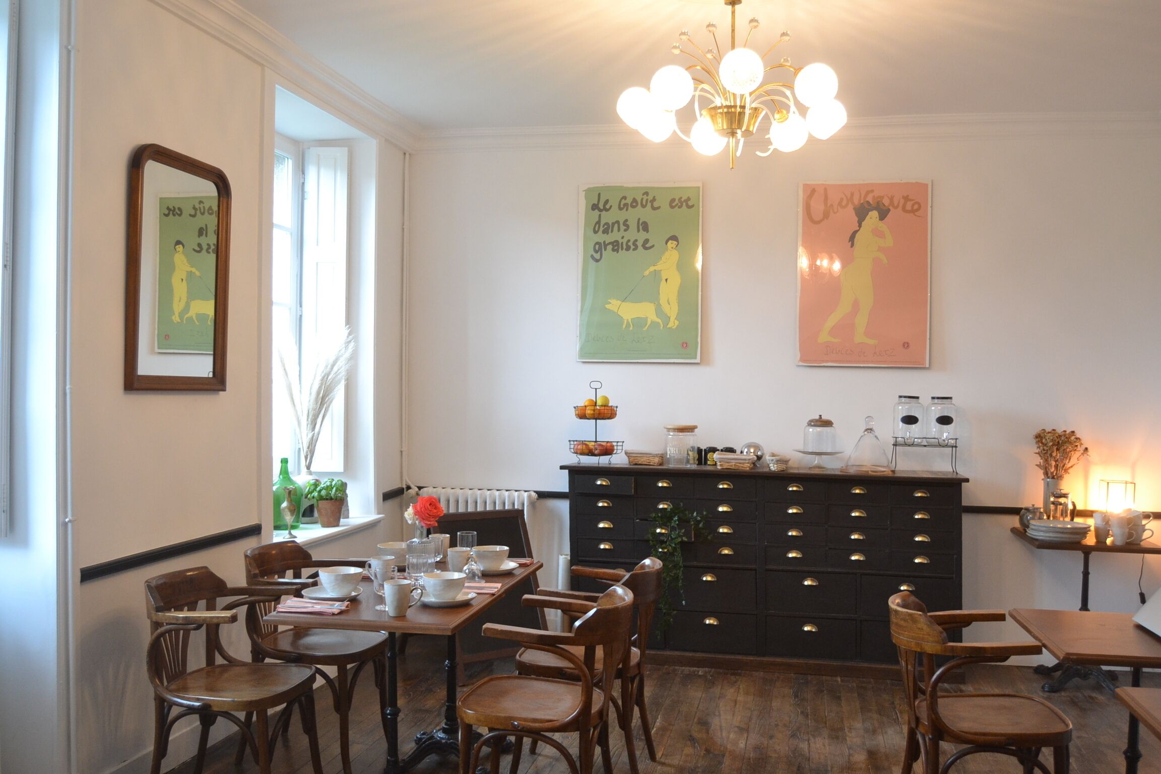 Een eetgedeelte met houten stoelen en tafels, een zwarte kast met lades, en wanddecoratie waarop honden staan afgebeeld.