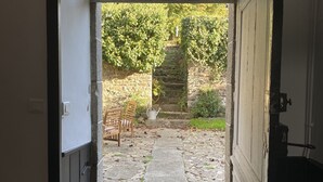 An open door leading to a stone pathway with a bench and a statue in a garden. - Artefact (Lamballe-Armor)