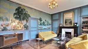 A room with a large mural, a fireplace, a yellow sofa, and a bookshelf. - Artefact (Lamballe-Armor)
