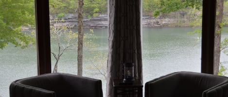 A room with two dark armchairs facing a window overlooking a lake and forest.