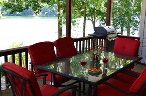 Una mesa con cubierta de vidrio, sillas rojas, una parrilla y vistas a un lago.
