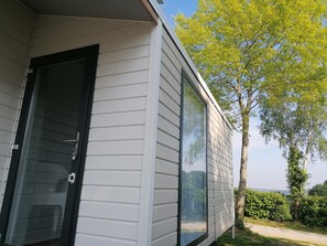 Uma casa moderna com janelas amplas, porta de correr de vidro e vista para uma árvore e vegetação.