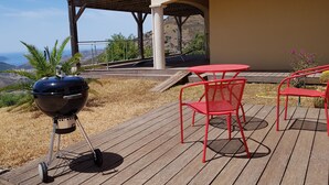 Eine Holzterrasse mit einem Grill, roten Metallstühlen und einem Tisch.