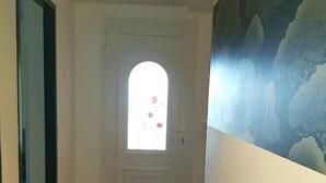 Ein Flur mit einer weißen Tür, einem Fenster mit Blick auf Blumen und einer Wand mit Blätermotiv.