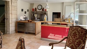 A spacious kitchen with a central island, a dining area with a red accent wall, and a large window providing natural light. - Villa Piscine Ardèche (Rochemaure)