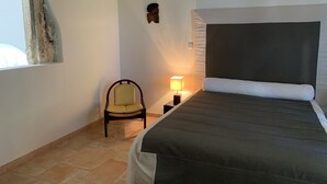 A bedroom with a bed, a chair, a nightstand with a lamp, a wall-mounted decoration, and a window. - Villa Piscine Ardèche (Rochemaure)