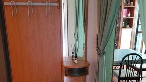 Una habitación con un armario de madera, un pequeño lavabo con espejo, una mesa de comedor con sillas y una cortina verde.