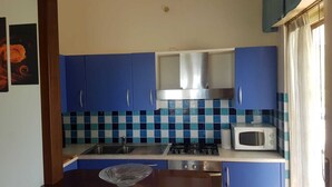 Una cocina compacta con armarios azules, una campana extractora de acero inoxidable, un microondas y una estufa a gas.