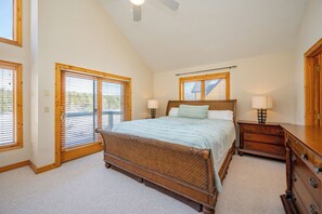 Quarto com uma cama grande, cabeceira de madeira, duas mesas de cabeceira com luminárias, cômoda de madeira e ventilador de teto.