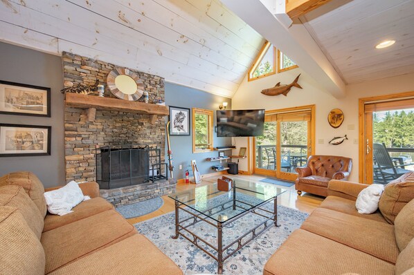 A spacious living room with a stone fireplace, leather sofas, a glass coffee table, and a large TV.