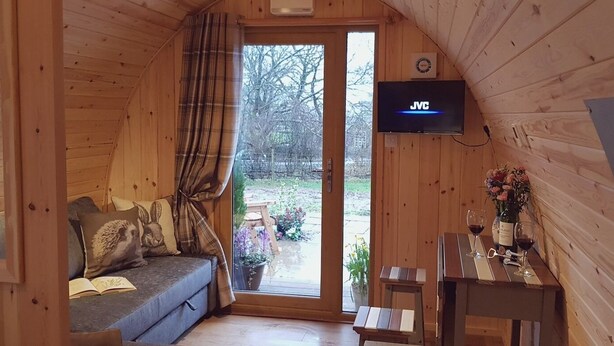 Een gezellig interieur van een vakantiehuisje met een bank, een tafel met een wijnglas en een aan de muur bevestigde televisie.