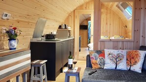 Een gezellig interieur van een blokhut met een kitchenette, een bank met decoratieve kussens en een kleine eettafel.
