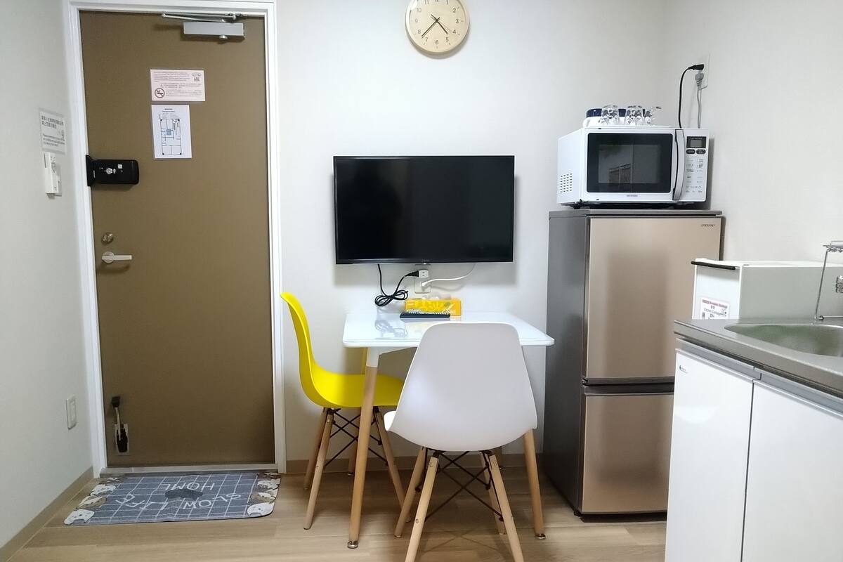A compact kitchen with a microwave, refrigerator, and a flat-screen TV on a white table.
