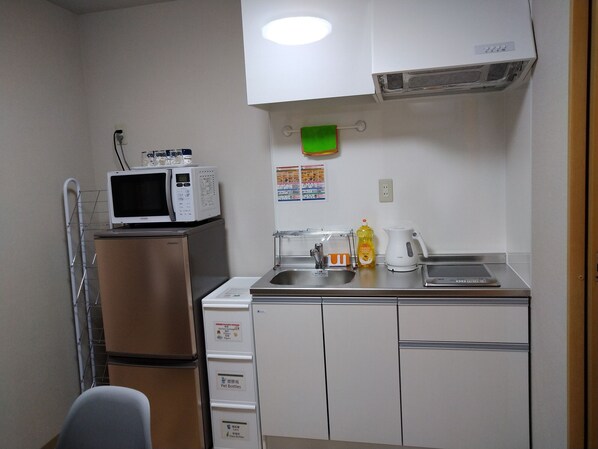 A compact kitchenette with a microwave on a small fridge, a sink with a soap dispenser, and a kettle.