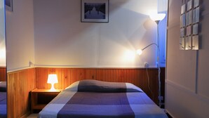 A hotel room with a wooden headboard, a bedside lamp, a framed picture on the wall, and a wall-mounted light fixture.