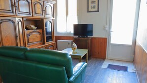 A green leather sofa, wooden cabinets, a television on a stand, and a small table with a decorative item.