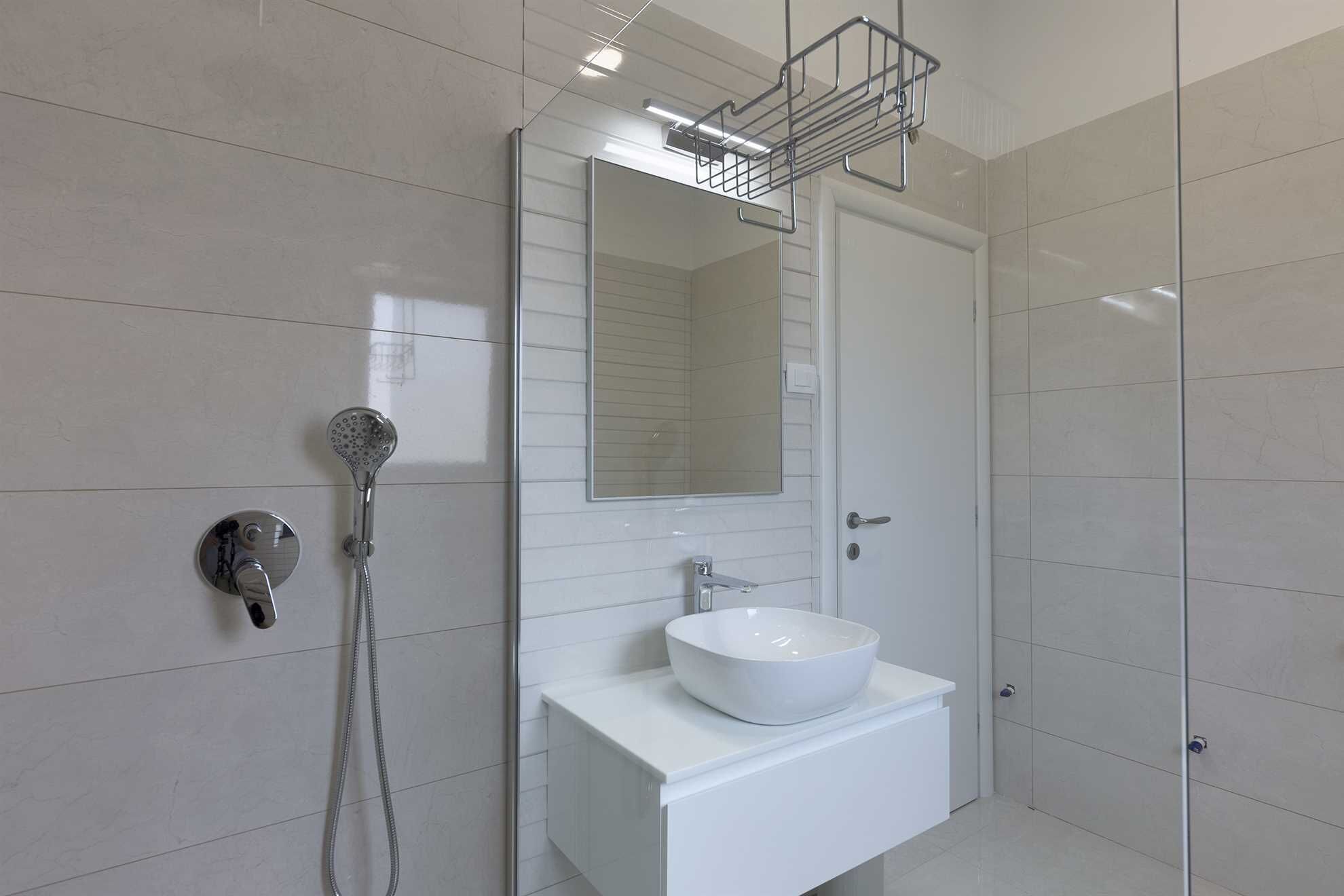 A modern bathroom with a white sink, a handheld showerhead, and a mirror above the sink.