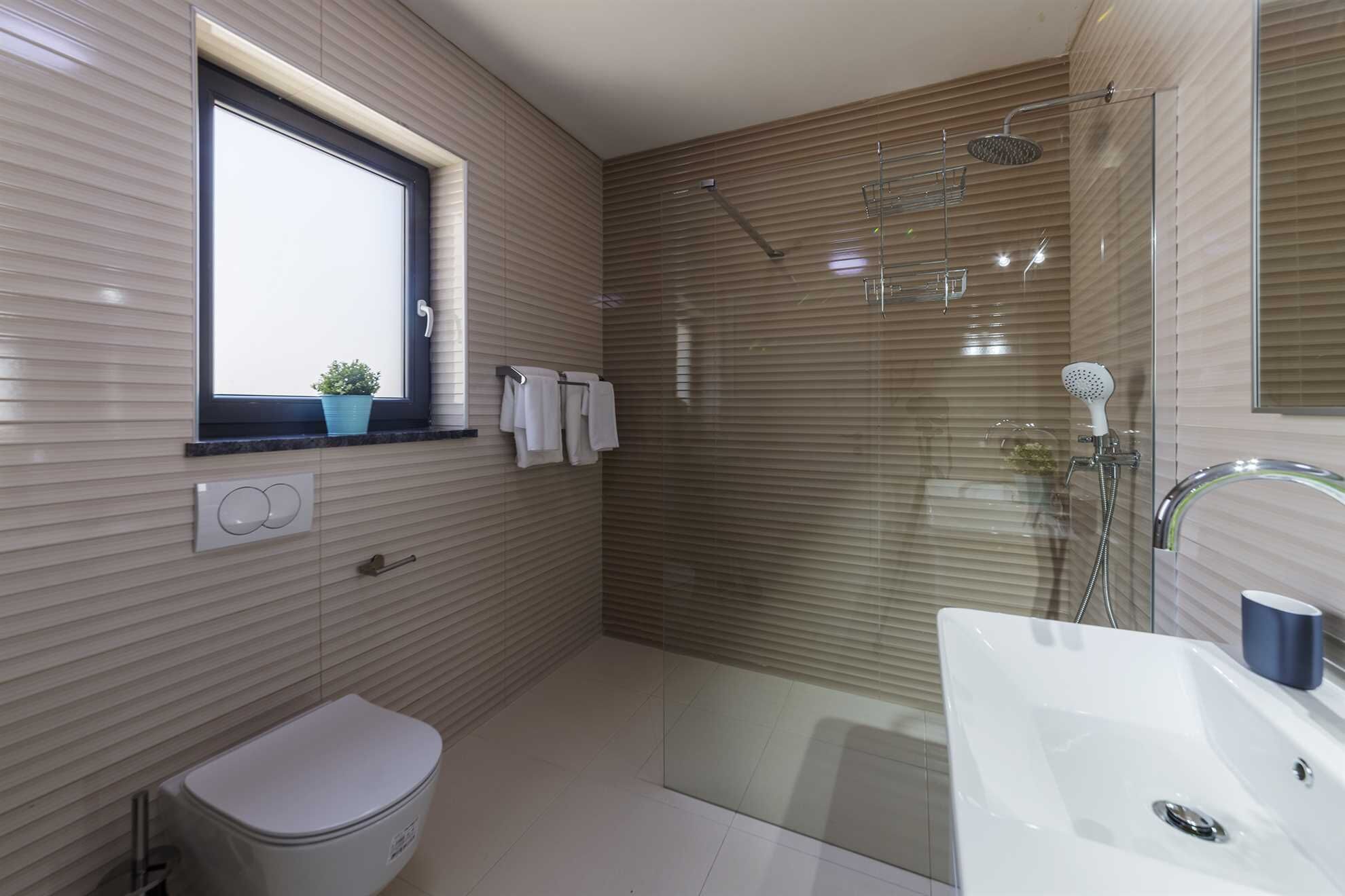 Un baño moderno con inodoro, lavamanos, ducha y ventana con persianas.