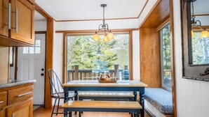 A wooden dining table with benches, a chandelier, and a view of a deck with trees.