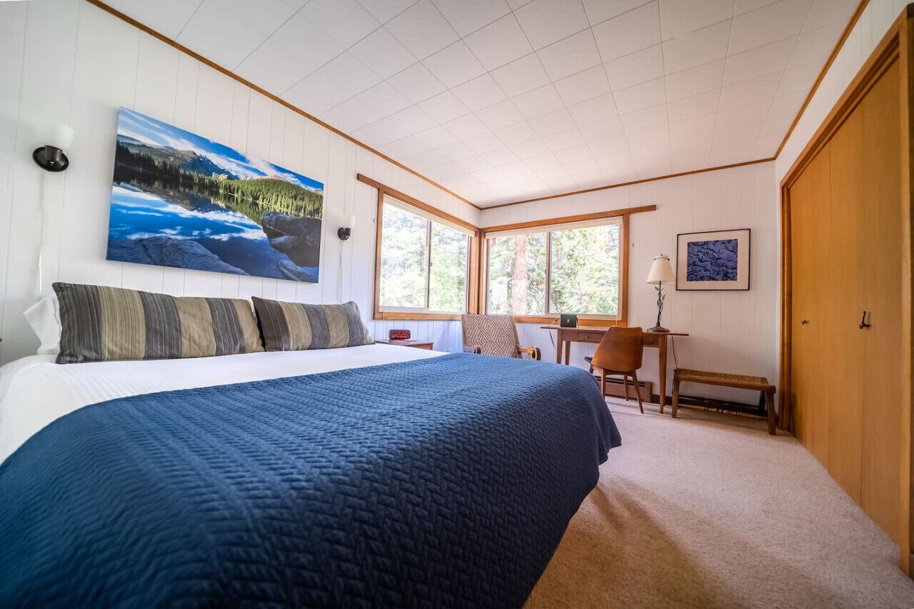 Ein Schlafzimmer mit einem großen Bett, einem Schreibtisch und einem Stuhl, einem Gemälde an der Wand und einem Fenster mit Blick auf Bäume.
