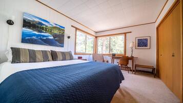 Ein Schlafzimmer mit einem großen Bett, einem Schreibtisch und einem Stuhl, einem Gemälde an der Wand und einem Fenster mit Blick auf Bäume.