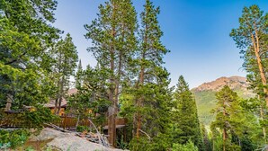 A lodge surrounded by tall pine trees and rocky terrain with a mountain in the background.