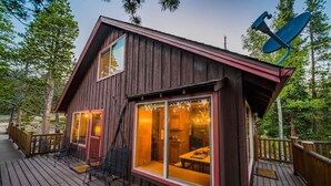A wooden cabin with a deck, large windows, and a satellite dish.