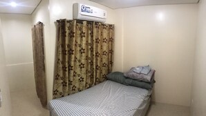A small, simple room with a bed, a pillow, a blanket, and a wall-mounted air conditioner. - Your Home Away From Home (Talisay)
