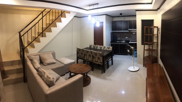 A modern living room with a sofa, dining table, and chairs, a staircase, and a kitchen area. - Your Home Away From Home (Talisay)