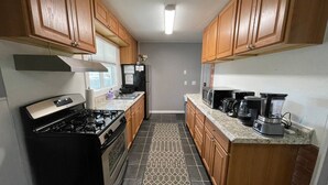 Una cocina compacta con armarios de madera, cocina a gas, refrigerador, microondas, cafetera y licuadora.