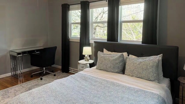 Un dormitorio con cama, escritorio, silla, mesita de noche, lámpara y ventilador de techo.
