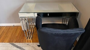 Un escritorio moderno con superficie de vidrio y una silla negra.