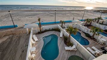 A pool area with multiple pools, lounge chairs, and a view of the beach.