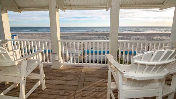 A wooden deck with white railings and two white Adirondack chairs facing a beach. - Ocean Front Ocean View, With Private Heated Pool & Hot Tub (Atlantic Beach)