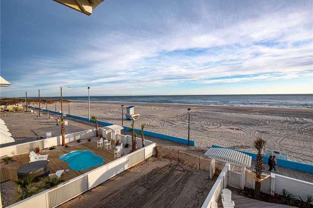 Blick auf einen Strand mit Swimmingpool, Liegestühlen und einem eingezäunten Bereich.