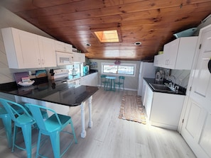A compact kitchen with white cabinets, a black countertop, and turquoise chairs.