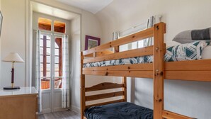 Un letto a castello con struttura in legno e materasso scuro, un comodino con lampada e una finestra con tende.