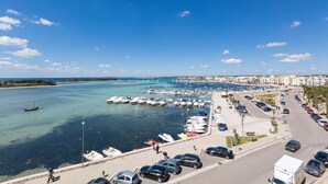 A marina with boats docked, a parking area, and a coastal cityscape in the background.