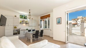 A modern apartment with a dining area, kitchenette, and a large window.