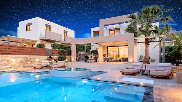 A modern outdoor pool area with a clear night sky, a stone wall, and lounge chairs.